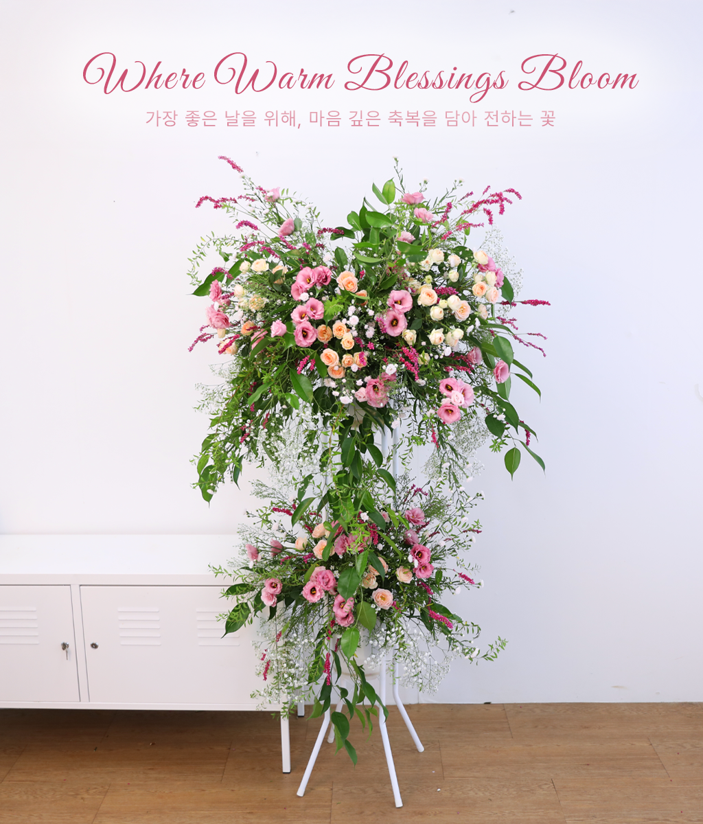 <br>Where Warm Blessings Bloom<br>
부드러운 핑크 계열의 꽃을 중심으로 구성한 플라워 스탠드입니다.
연한 살몬핑크와 크림 톤의 꽃이 자연스럽게 어우러지며, 잎 소재를 충분히 사용해 전체적인 볼륨과 균형을 잡았습니다.